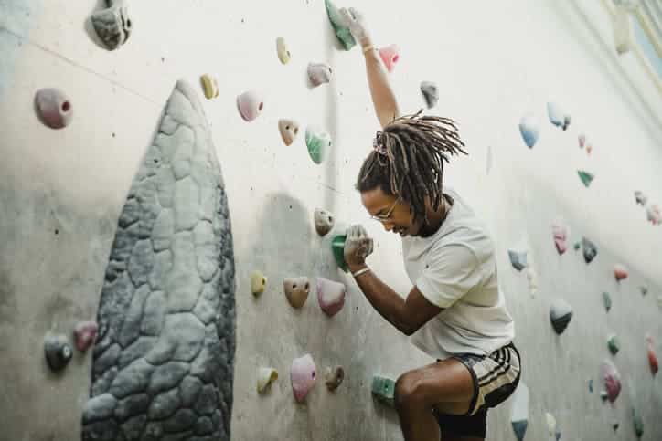 Afroamerikaner mit langen Dreadlocks grinsend beim Klettern und Bouldern in Halle im Wetteraukreis